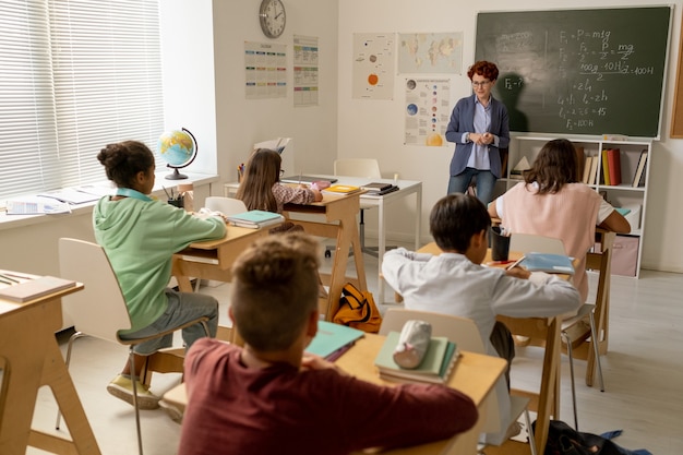 Junge Lehrerin, die vor interkulturellen Schulkindern an der Tafel steht