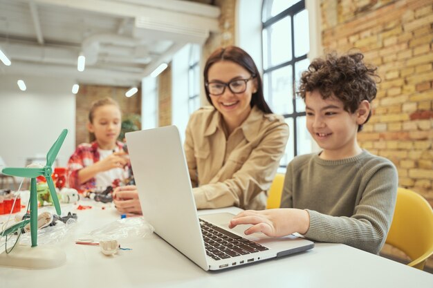 Junge Lehrerin mit Brille mit Laptop im Klassenzimmer, die wissenschaftliches Robotik-Video zeigt