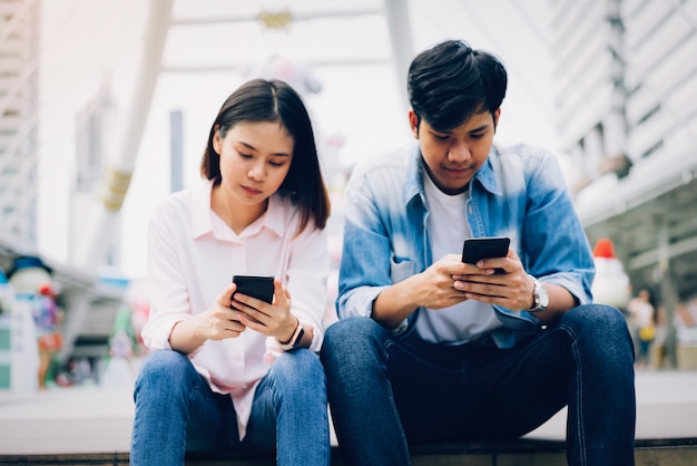 Junge Leute benutzen Smartphone und lächeln beim Sitzen auf Freizeit. Technologiekonzept