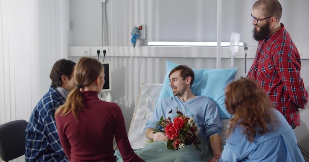 Junge Leute besuchen einen Freund im Krankenhaus und bringen Blumen