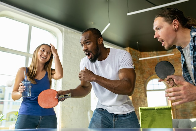 Junge Leute, die am Arbeitsplatz Tischtennis spielen, Spaß haben