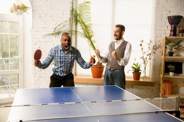 Junge Leute, die am Arbeitsplatz Tischtennis spielen und Spaß haben