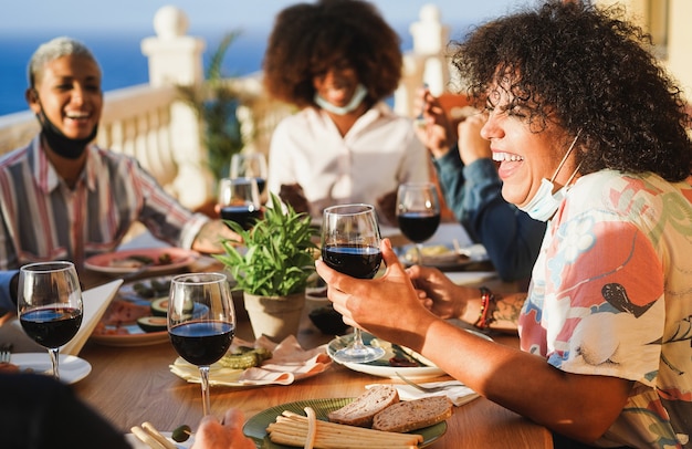 Junge Leute, die Rotwein essen und trinken, während sie Schutzmasken tragen