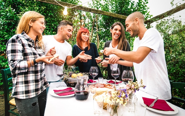 Junge Leute, die Spaß daran haben, lokales Essen zu essen und Rotwein beim Gartenfest auf dem Land zu trinken - Freundschafts- und Lebensstilkonzept mit glücklichen Freunden zusammen auf der Bauernhof-Terrassenparty - Warmer, lebendiger Filter