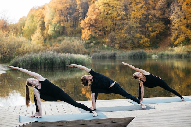 Junge Leute, die Yoga Asana in der Natur nahe dem See tun