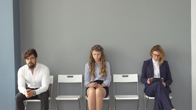 Junge Leute erwarten Interviews auf Stühlen in einem Bürogebäude. das Interview für den Job. Rekruten sind gelangweilt und genießen die Geräte.