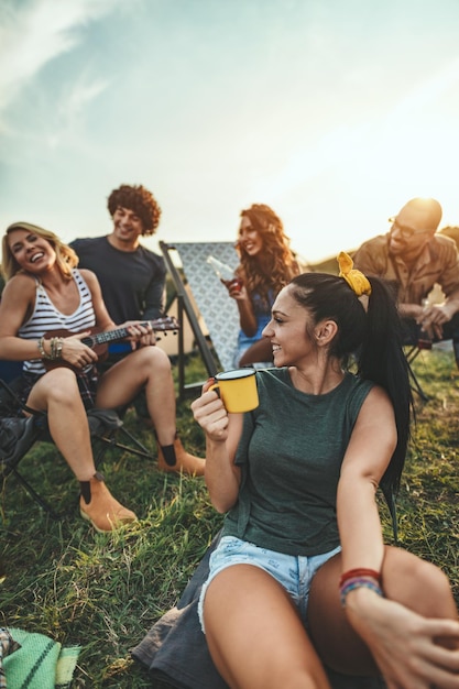 Junge Leute haben eine gute Zeit im Camp in der Natur. Sie ruhen sich aus, lachen und singen zu Ukulelenmusik und sind glücklich, zusammen zu sein.