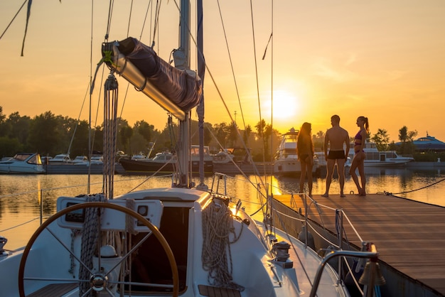 Junge Leute in der Nähe der Segelyacht Yacht bei Sonnenuntergang Typ mit den Mädchen am Kai in der Nähe des Segelns