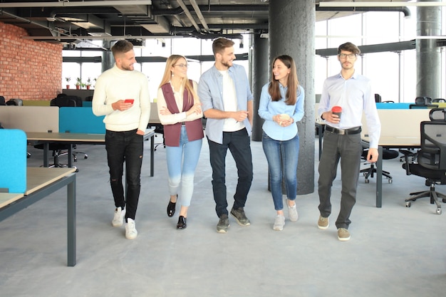 Junge Leute in eleganter Freizeitkleidung diskutieren über das Geschäft und lächeln, während sie durch das Büro gehen.