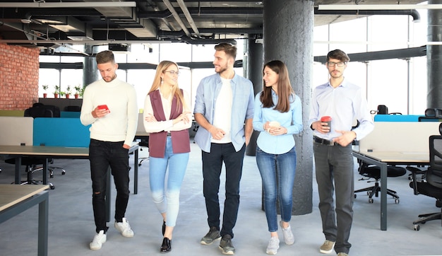 Junge Leute in eleganter Freizeitkleidung diskutieren über das Geschäft und lächeln, während sie durch das Büro gehen.