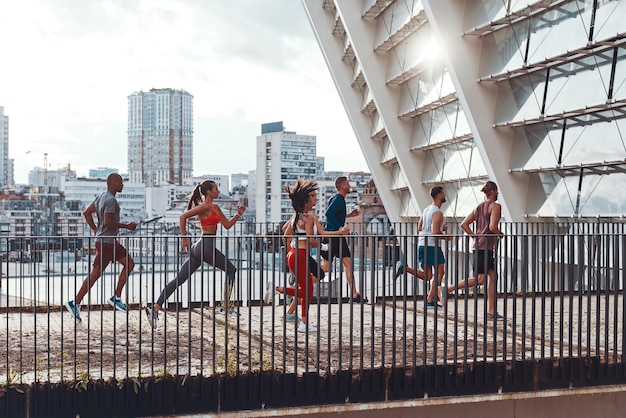 Junge Leute in Sportkleidung joggen in voller Länge beim Training auf der Brücke im Freien