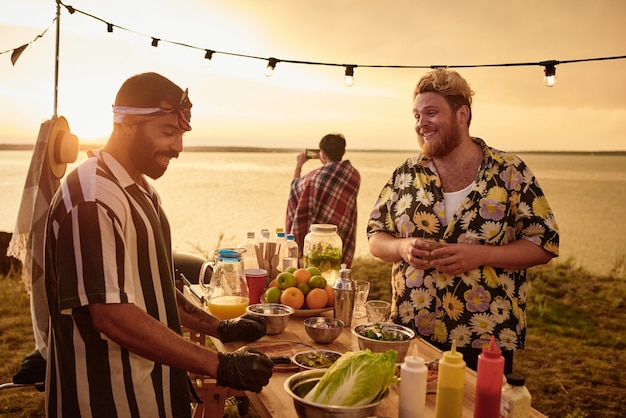 Junge Leute reden miteinander und essen Fast Food bei Sonnenuntergang auf einer Party am Strand