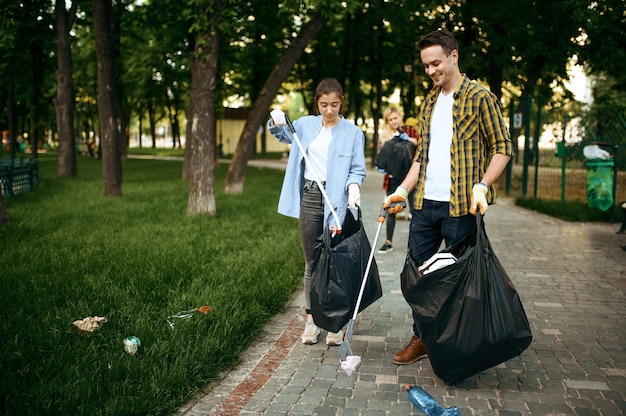 Junge Leute sammeln Müll in Plastiktüten im Park und melden sich freiwillig. Freiwillige reinigen Wald, ökologische Wiederherstellung, Müllabfuhr und Recycling, ökologische Pflege, Umweltreinigung