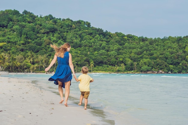 Junge liebevolle Mutter und ihr kleiner Sohn spielen am Strand