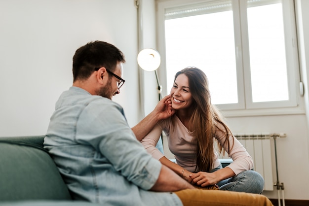 Junge liebevolle sprechende Paare beim Sitzen auf dem Sofa.