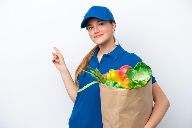 Junge Lieferfrau, die eine Tüte mit Essen zum Mitnehmen nimmt, isoliert auf weißem Hintergrund, die mit dem Finger zur Seite zeigt