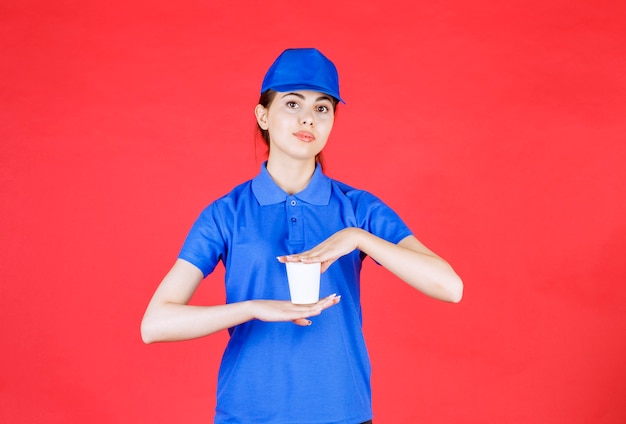 Junge Lieferfrau in blauer Kappe, die Plastiktasse Tee auf Rot hält.