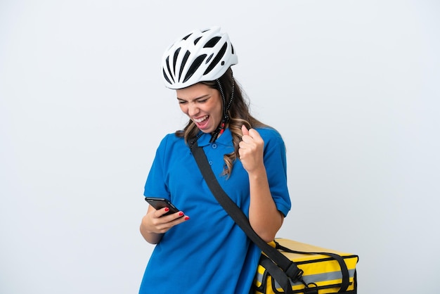 Junge Lieferfrau mit Thermorucksack isoliert auf weißem Hintergrund mit Telefon in Siegesposition