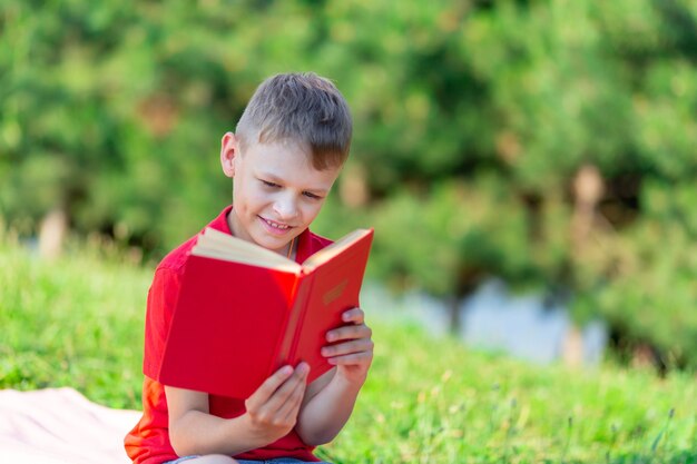 Junge liest ein Buch im Park vor einem grünen Hintergrund