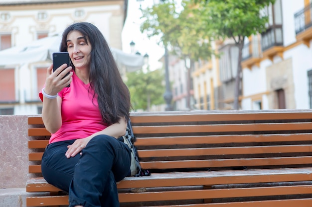 Junge Lifestyle-Stadtmenschen, die auf einer Straßenbank sitzen und ihr Handy bei Videoanrufen benutzen