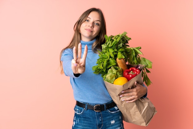 Junge litauische Frau, die eine Einkaufstasche des Lebensmittels glücklich hält und drei mit den Fingern zählt