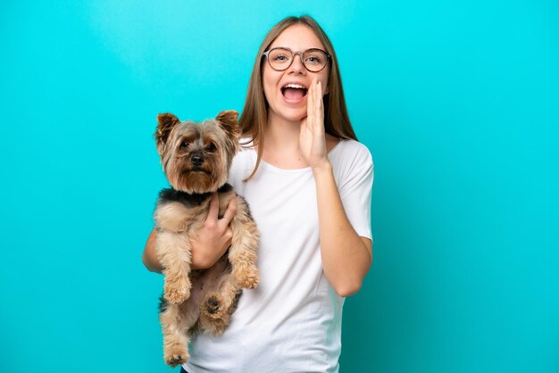 Junge litauische Frau, die einen Hund isoliert auf blauem Hintergrund hält und mit weit offenem Mund schreit