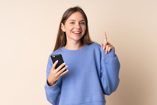 Junge litauische Frau, die Handy verwendet, lokalisiert auf beigem Hintergrund, der eine große Idee aufzeigt