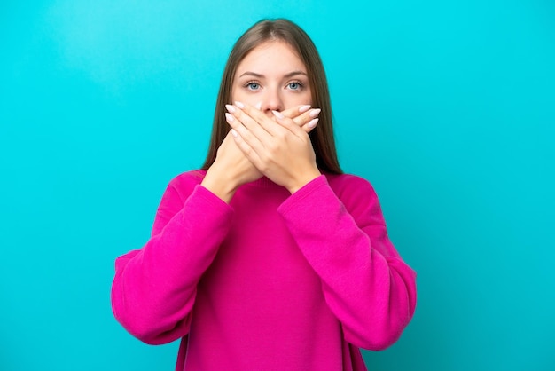 Junge litauische Frau isoliert auf blauem Hintergrund, die den Mund mit den Händen bedeckt