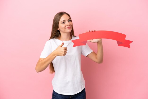 Junge litauische Frau isoliert auf rosafarbenem Hintergrund, die ein leeres Plakat mit erhobenem Daumen hält