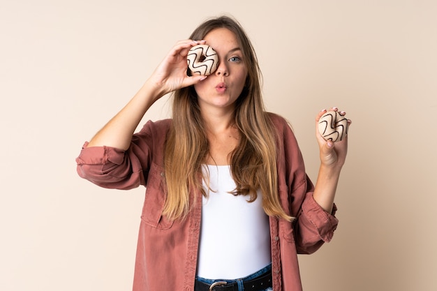 Junge litauische Frau lokalisiert auf Beige, die einen Donut in einem Auge hält