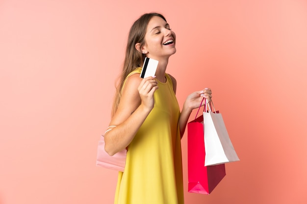 Junge litauische Frau lokalisiert auf rosa, die Einkaufstaschen und eine Kreditkarte hält