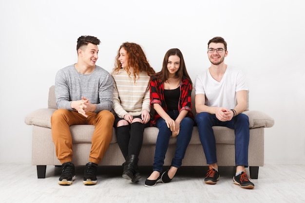 Junge lockere Leute, fröhliche Freunde, die reden, Spaß haben, drinnen auf der Couch sitzen und lachen