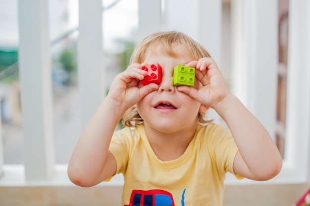 Junge macht Augen aus bunten Kinderblöcken. Netter kleiner Junge mit Brille, die mit vielen bunten Plastikblöcken innen spielt. Förderung von Fähigkeiten und Kreativität