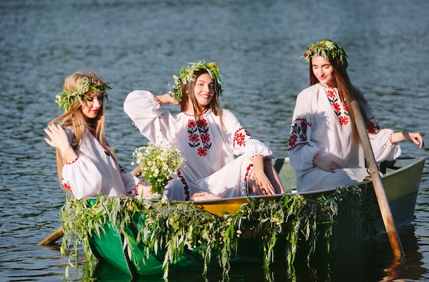 Junge Mädchen in Trachten segeln in einem Boot, das mit Blättern und Pflanzen geschmückt ist. Slawischer Feiertag von Ivan Kupala.