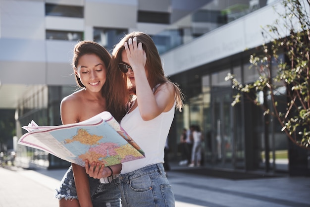 Junge Mädchen lesen Stadtplan und suchen nach Hotel. Schöne Touristen mit Rucksäcken bestimmen das Konzept des Wissens über die Welt