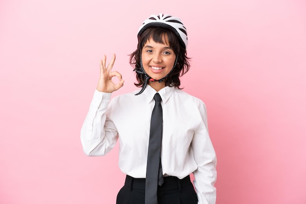 Junge Mädchen mit einem Fahrradhelm isoliert auf rosa Hintergrund, der mit den Fingern ein Ok-Zeichen zeigt