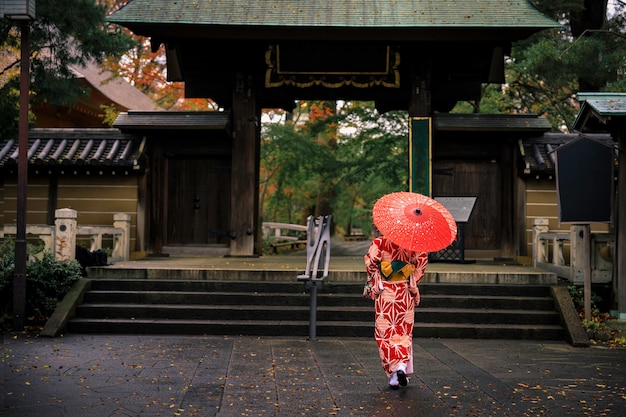 Foto junge mädchen tourist tragen roten kimono und regenschirm machte einen spaziergang im parkeingang in der herbstsaison in japan