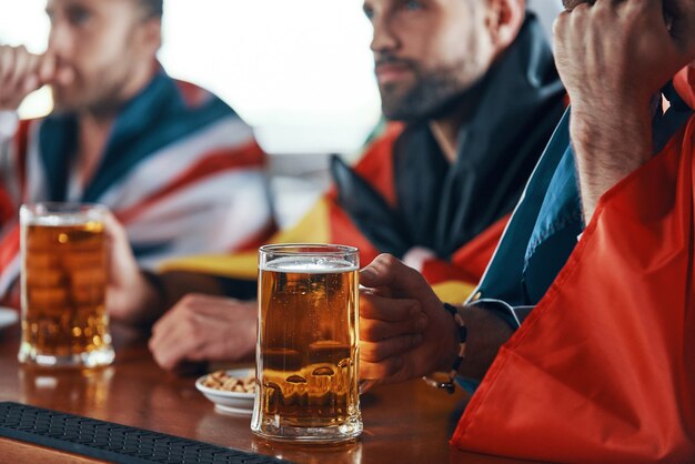 junge Männer, die mit internationalen Flaggen bedeckt sind, genießen Bier