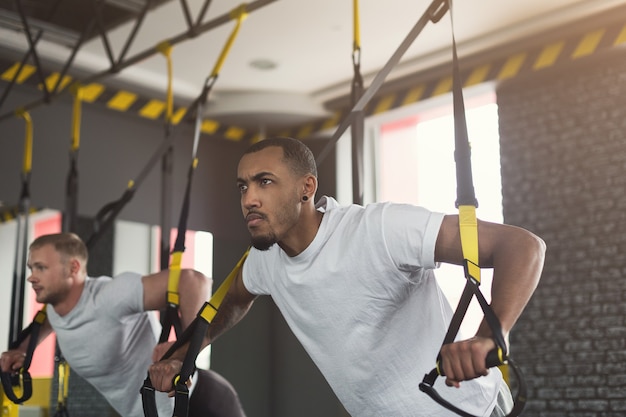 Junge Männer, die TRX-Training im Fitnessstudio durchführen. Muskulöse Jungs, die mit elastischem Seil trainieren, Platz kopieren