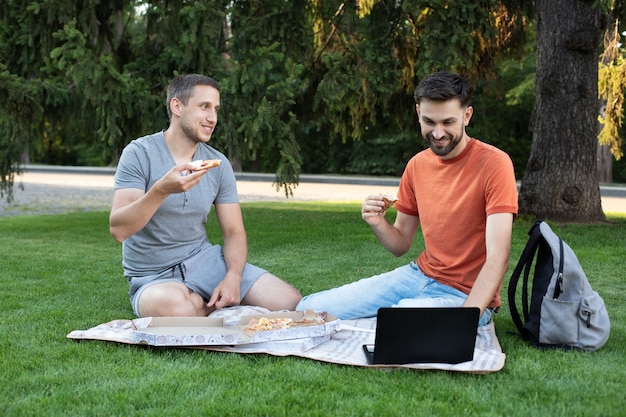 Junge Männer essen leckere Pizza, reden und lachen über Witze