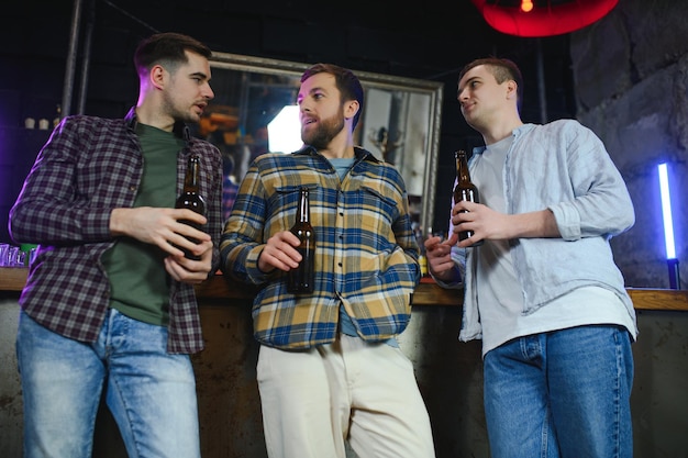 Junge Männer in Freizeitkleidung unterhalten sich lachend und trinken, während sie an der Bartheke in der Kneipe sitzen