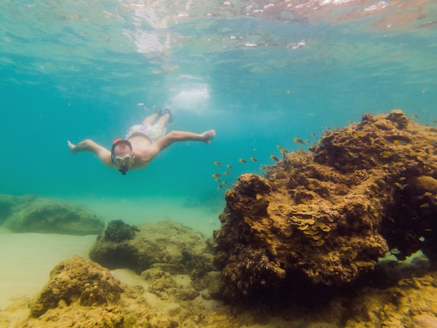 Junge Männer schnorcheln beim Erkunden der Unterwasserkorallenrifflandschaft im tiefblauen Ozean mit bunten Fischen und Meereslebewesen