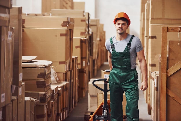 Junge männliche Arbeiter in Uniform sind mit Hubwagen im Lager.