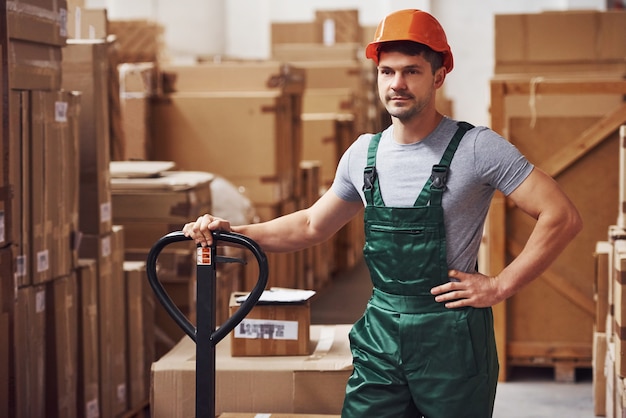 Junge männliche Arbeiter in Uniform sind mit Hubwagen im Lager.