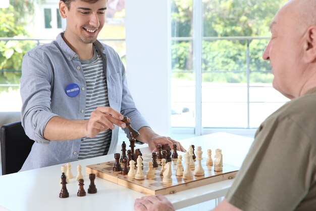 Junge männliche Freiwillige, die Schach mit einem älteren Mann im hellen Raum spielen