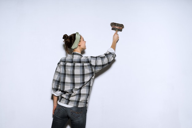 Junge Malerin in einem karierten Hemd malt eine Wandbürste, repariert in einer neuen Wohnung