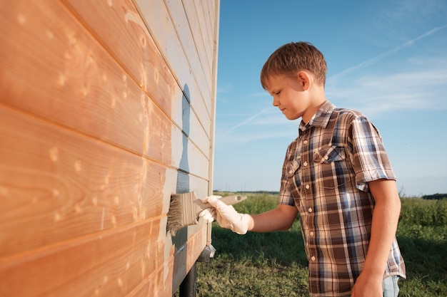 Junge malt die Wand eines Holzhauses. Sohn hilft Eltern beim Streichen des Gartenhauses