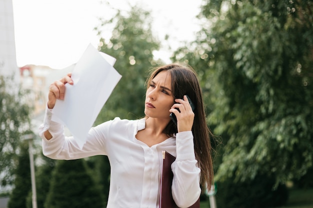 Junge Managerin hält Blätter Papier, die draußen in der Stadt am Telefon sprechen. Alles im Geschäft