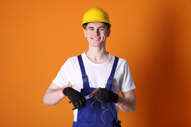 Junge Mann mit Zangen und Drähten auf orangefarbenem Hintergrund