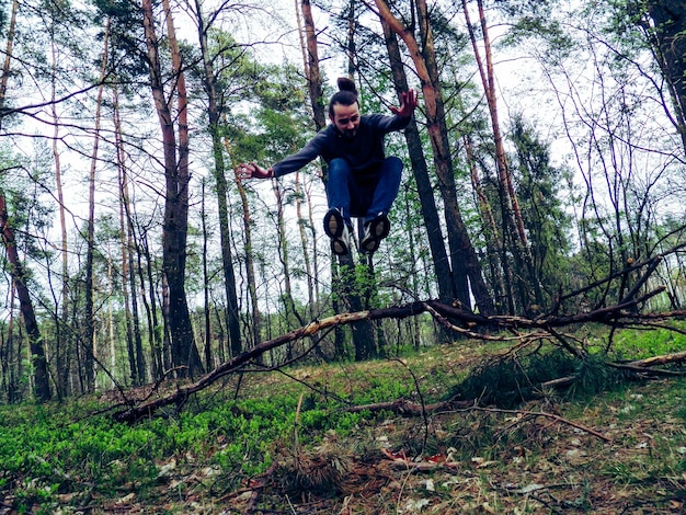 Junge Mann springt über gebrochene Zweige gegen Bäume im Wald